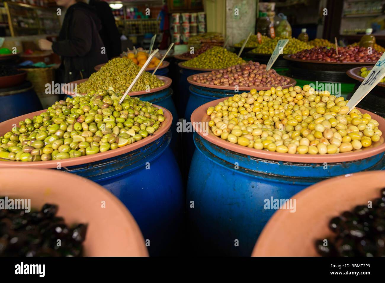 Verschiedene grüne, gelbe und schwarze Oliven in Tonschalen auf Fässern in einem lokalen marokkanischen Souk, perfekt für kulinarische Themen Stockfoto