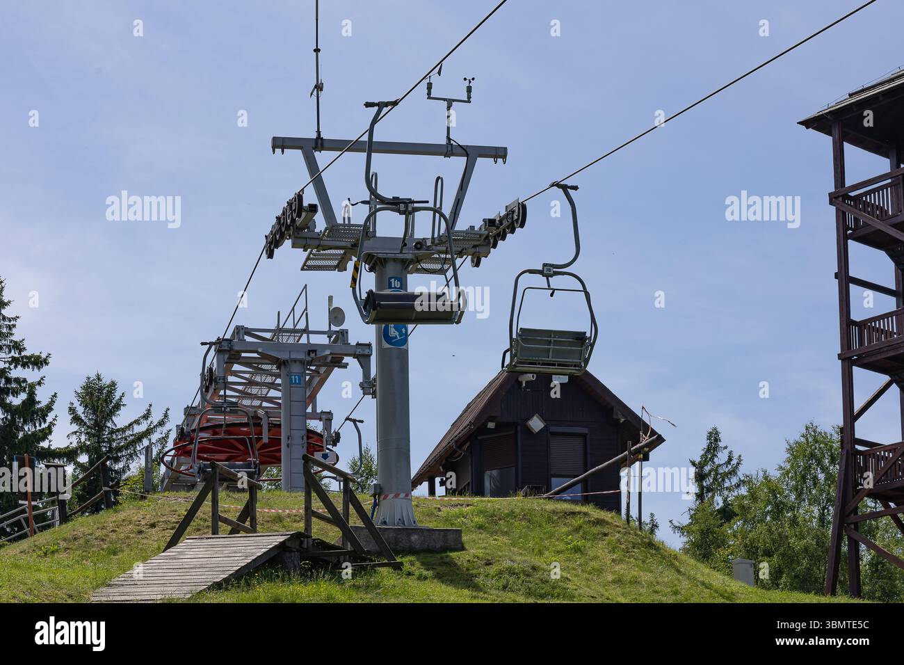 Modernes Seilbahnsystem mit technischem Turm und Stützinfrastruktur auf grüner Sommerpiste. Verkehrstechnik und -Technik Stockfoto