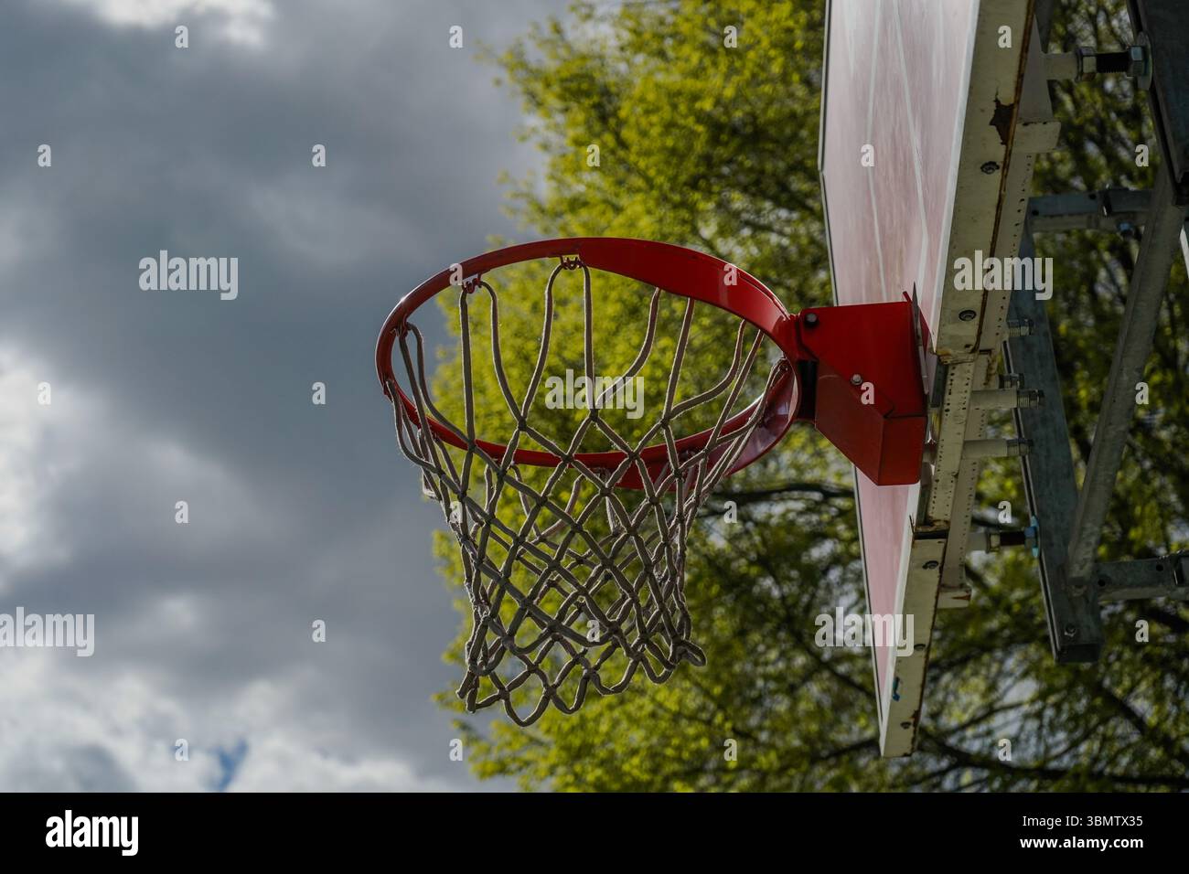 Nahaufnahme eines Basketballkörpers, zentriert im Rahmen. Der rote Rand des Rings und die orange lackierte Rückwand sind sichtbar, während das Netz in der Sonne leuchtet Stockfoto