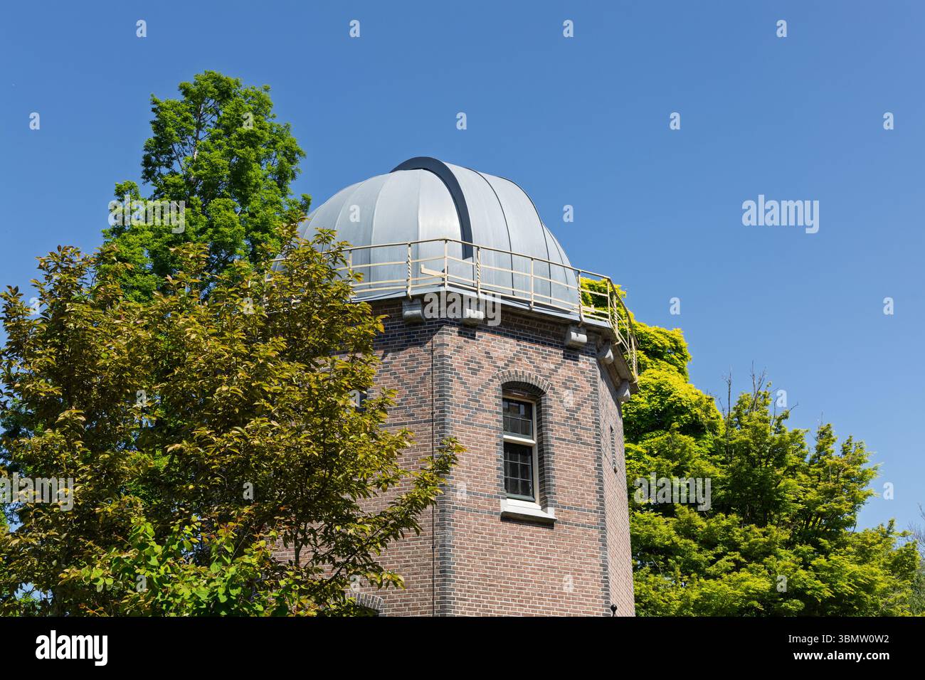 Die historische Kuppel des Leiden Observatoriums erstrahlt in einem klaren blauen Himmel, umgeben von üppigen grünen Bäumen. Ein Symbol der wissenschaftlichen Entdeckung. Stockfoto