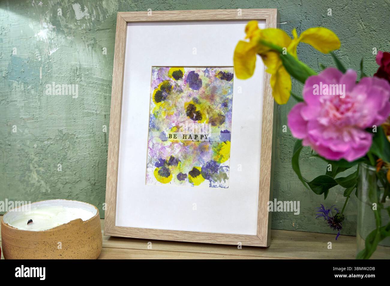 Gerahmter botanischer Druck mit „Be Happy“-Text im gemütlichen Innenraum – natürliche Blütenpigmente, handgefertigte Blumenkunstwerke, rustikale Wanddekoration Stockfoto