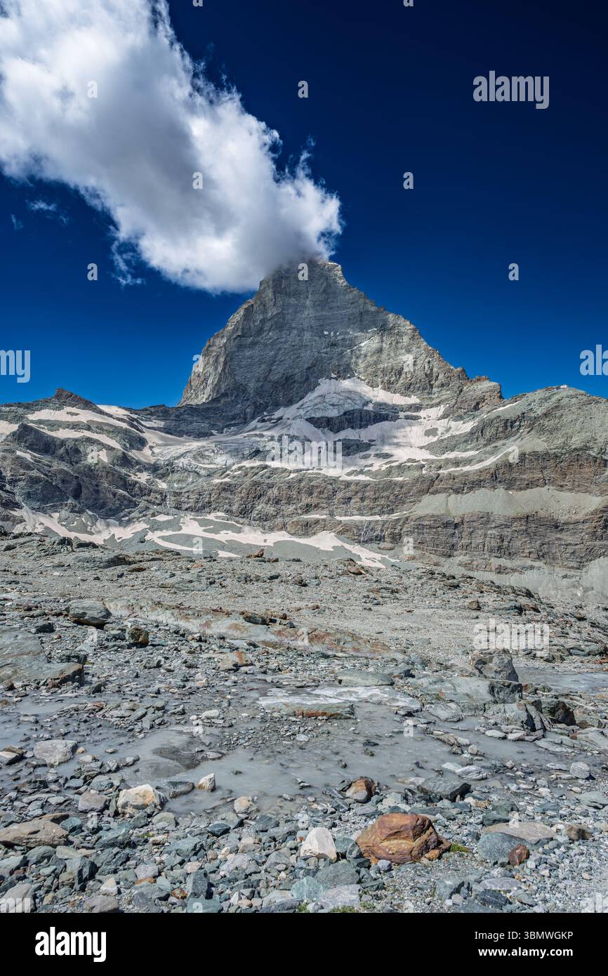 Das berühmte Matterhorn, teilweise von Wolken bedeckt, erhebt sich über eine felsige Landschaft mit Gletscherresten. Stockfoto