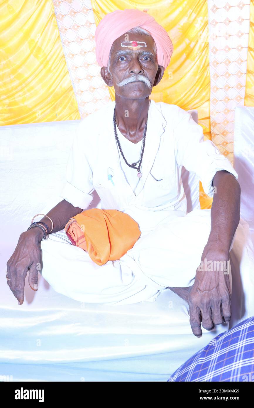 Älterer indischer Mann in traditioneller Kleidung mit Turban und Stirn tilak, der drinnen sitzt Stockfoto