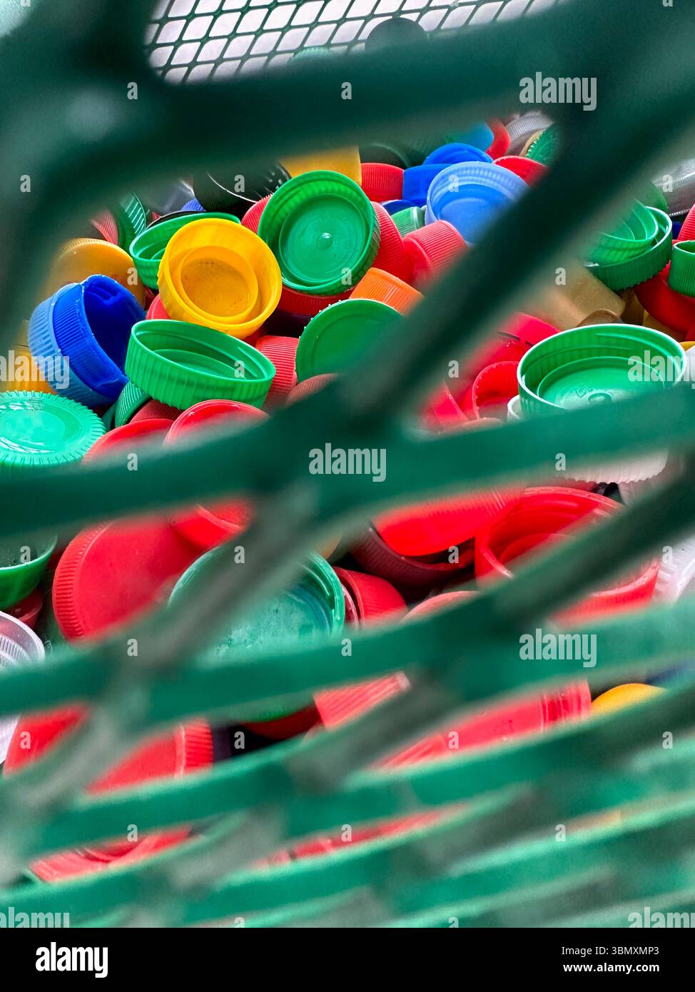 Farbenfrohe Plastikflaschenverschlüsse in einem geschlossenen Korb mit Netzen symbolisieren Recycling, Spende und Umweltschutz. Stockfoto