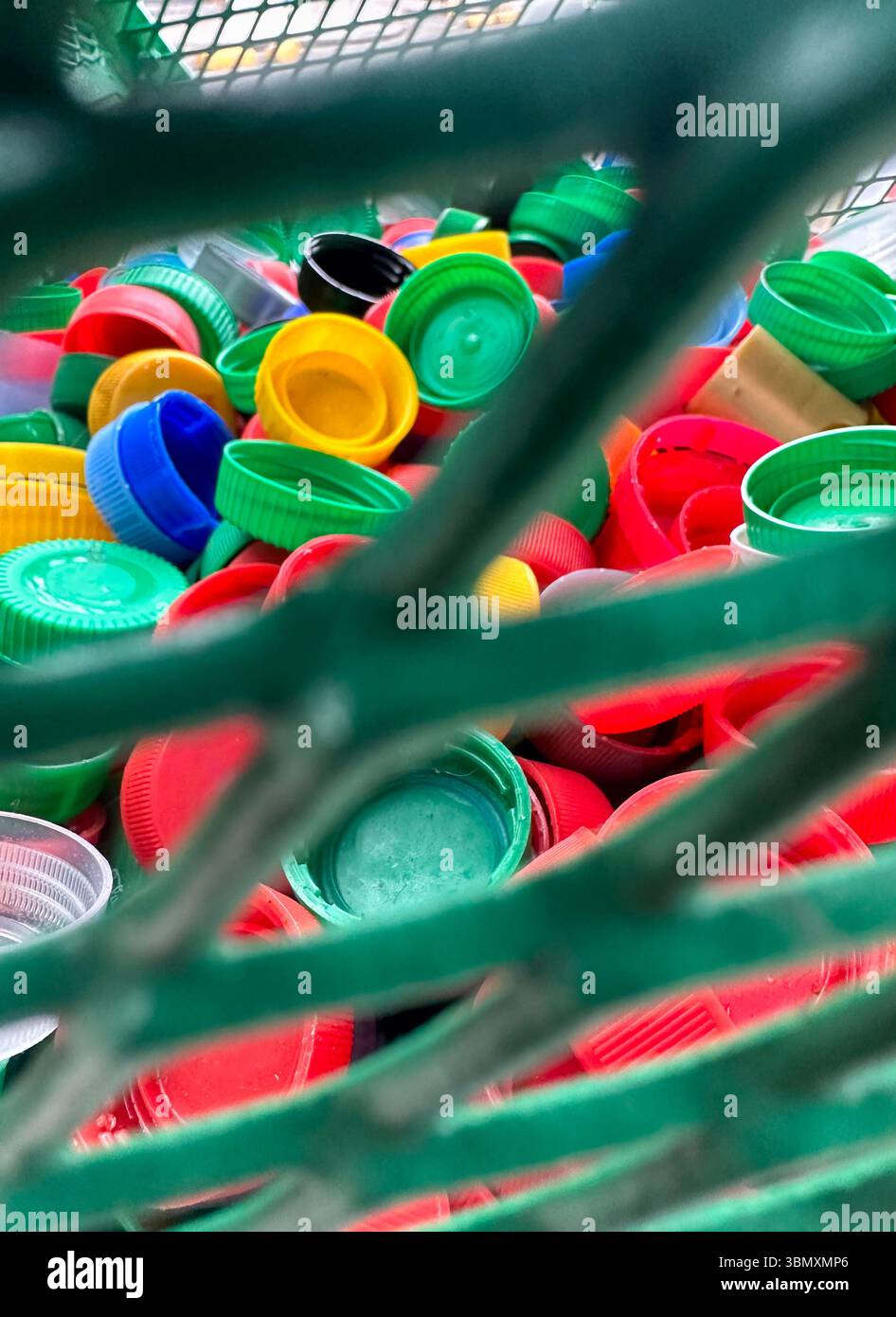 Farbenfrohe Plastikflaschenverschlüsse in einem geschlossenen Korb mit Netzen symbolisieren Recycling, Spende und Umweltschutz. Stockfoto