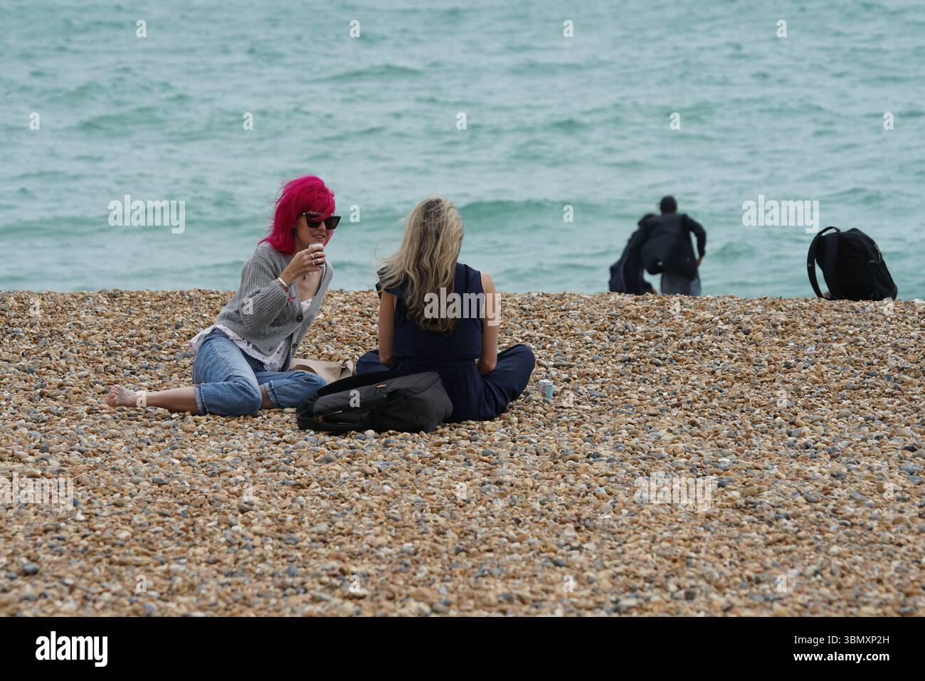 Zwei Freunde, die sich an einem Pebble Beach am Meer entspannen. Brighton, England Stockfoto