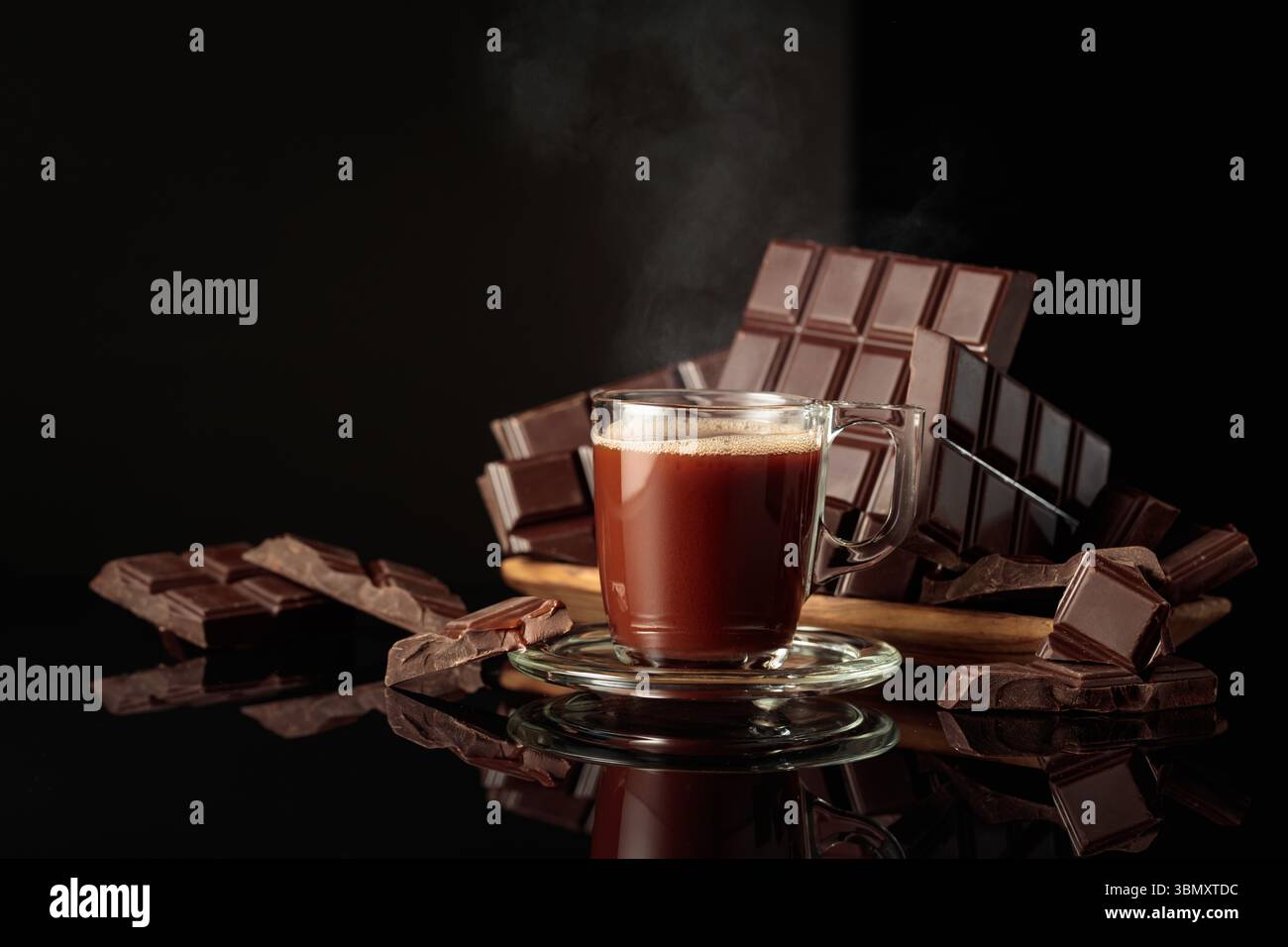 Tasse heiße Schokolade gegen zerbrochene Bitterschokoladentafeln. Der schwarze Hochglanzhintergrund sorgt für Tiefe und Reflexion. Kopierbereich. Stockfoto