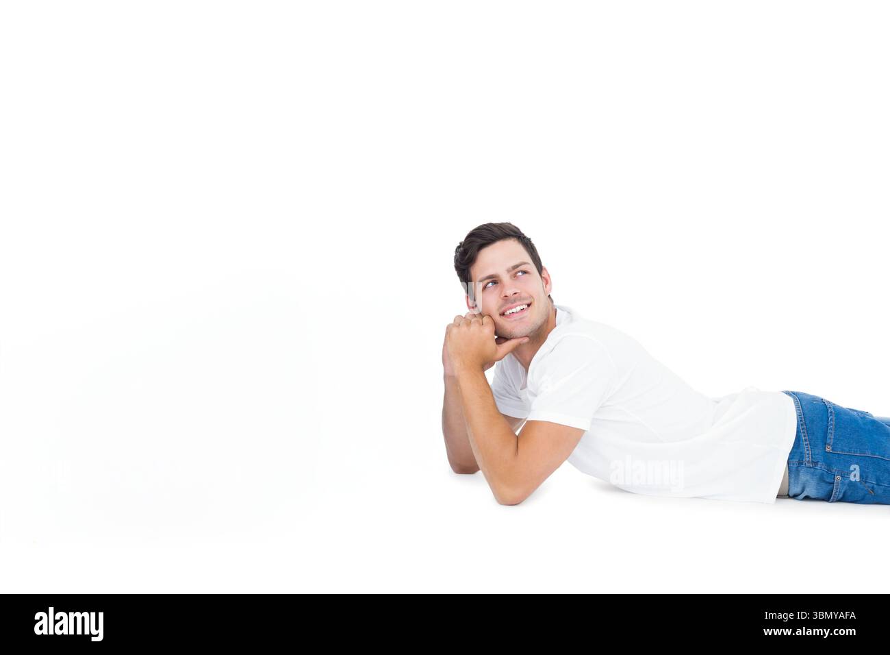 Mann, der auf dem Bauch liegt und Kopf auf den Händen im Studio stützt, mit weißem Hemd, Jeans, Kopierraum Stockfoto