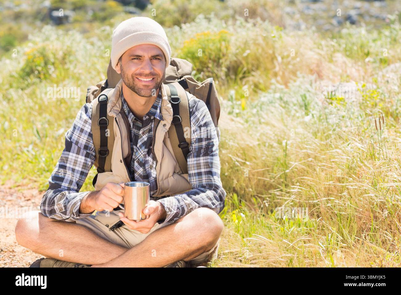 Mann, der im Kreuz auf dem Wanderweg sitzt und Wanderkleidung trägt, Edelstahlbecher hält Stockfoto