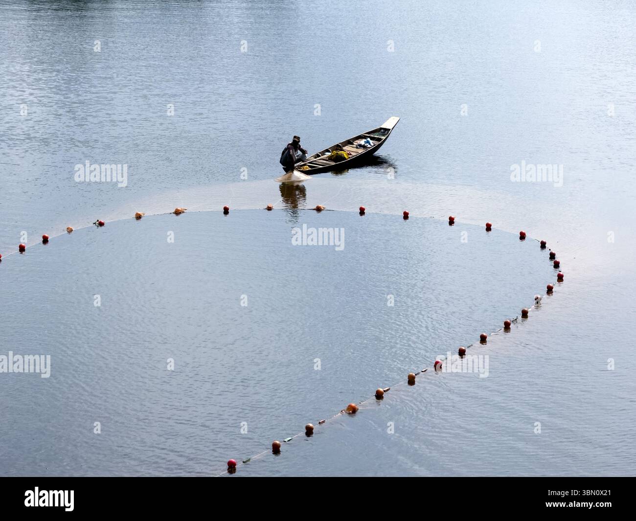 Fisherman Casting Net vom Holzboot in Kaptai Lake, Rangamati, Bangladesch – traditionelle Fischerei unterstützt die lokale Wirtschaft Stockfoto