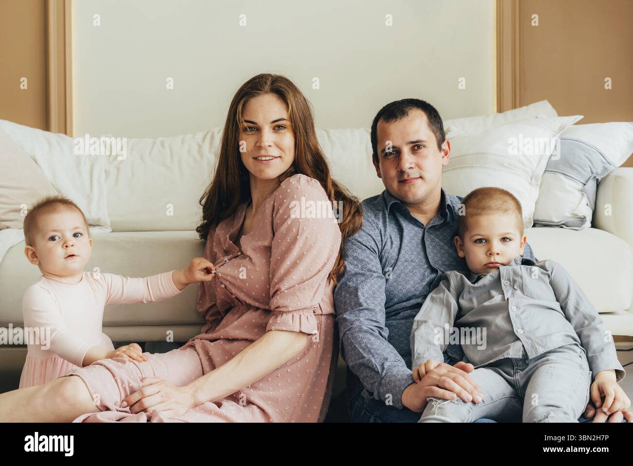 Glueckliche Mutter und Vater, die sich mit Tochter und Sohn umarmen, waehrend sie im Studio auf dem Boden sitzen Stockfoto