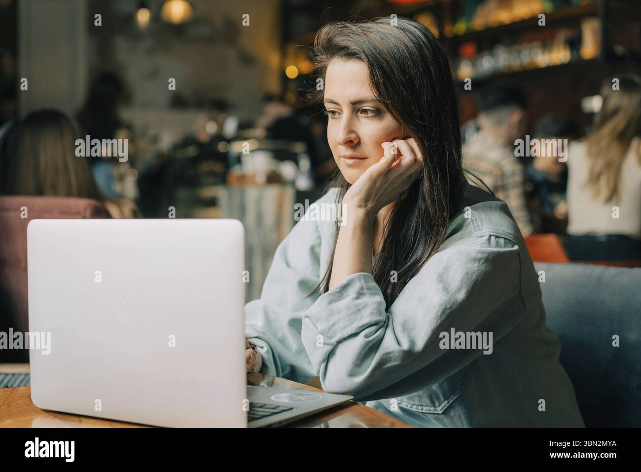 Eine junge Bruenette Frau sitzt in einem Cafe und arbeitet an einem Lapto Stockfoto