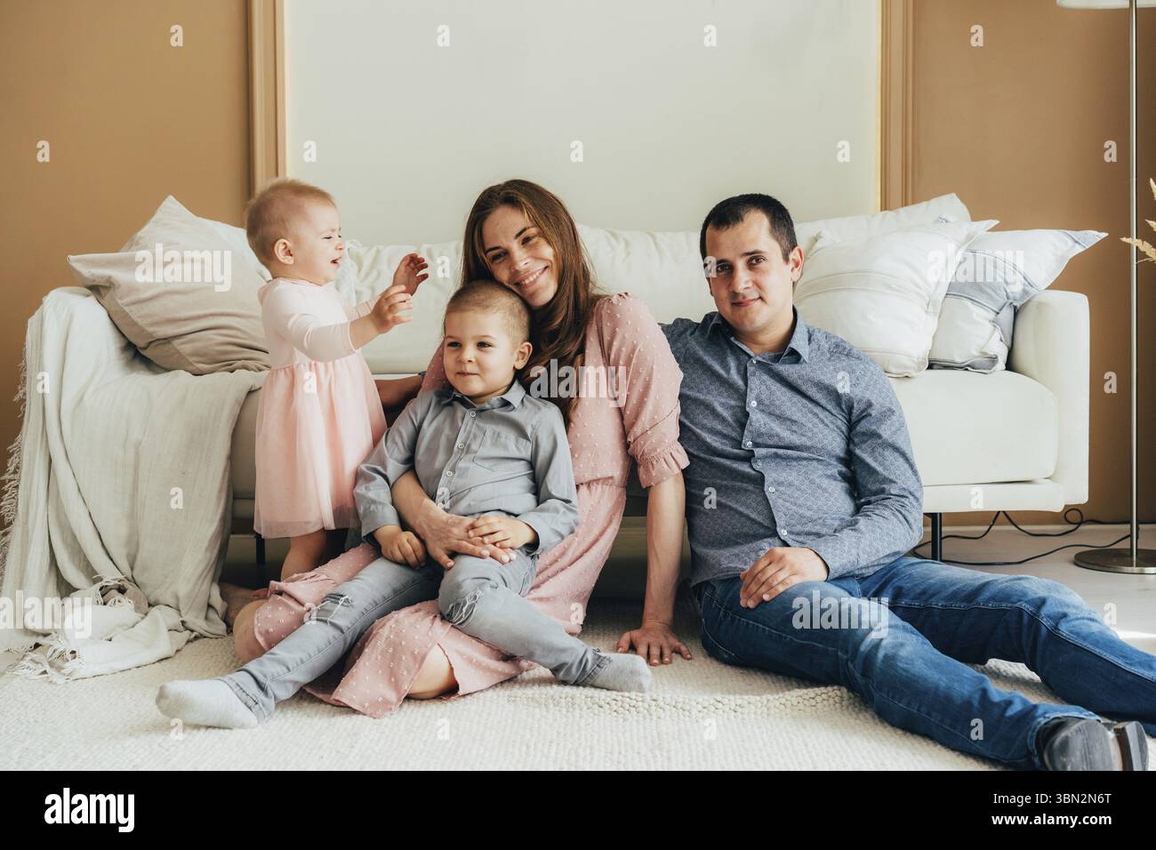 Junge glueckliche Eltern, die mit kleinen Kindern auf dem Boden sitzen und in die Kamera schauen Stockfoto