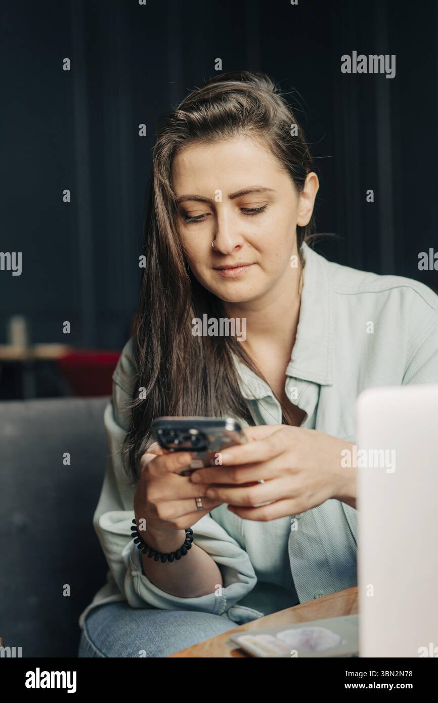 Eine junge Bruenette Frau sitzt in einem Cafe und surft mit einem Mobiltelefon im Internet Stockfoto