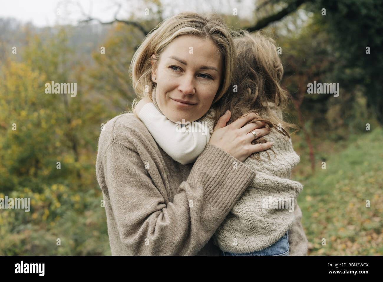 Junge huebsche Mutter, die kleine Tochter umarmt Stockfoto