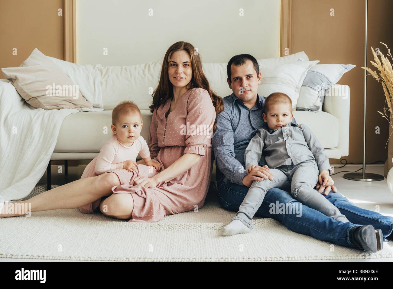 Glueckliche Mutter und Vater, die sich mit Tochter und Sohn umarmen, waehrend sie im Studio auf dem Boden sitzen Stockfoto