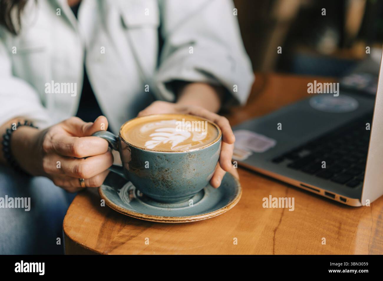 Frauenhände halten eine große Tasse mit Cappuccino am Tisch im Café Stockfoto