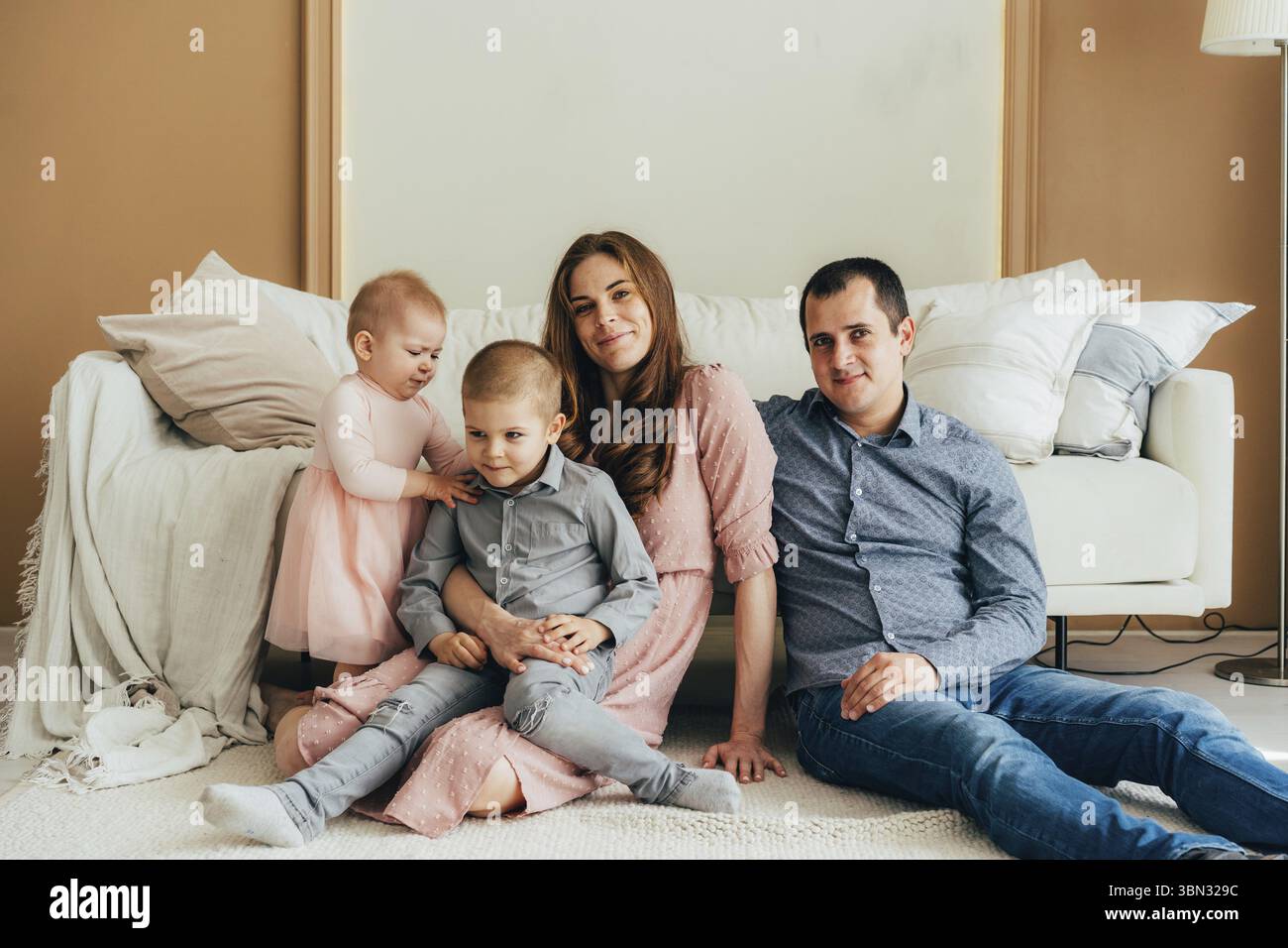 Junge glueckliche Eltern, die mit kleinen Kindern auf dem Boden sitzen und in die Kamera schauen Stockfoto