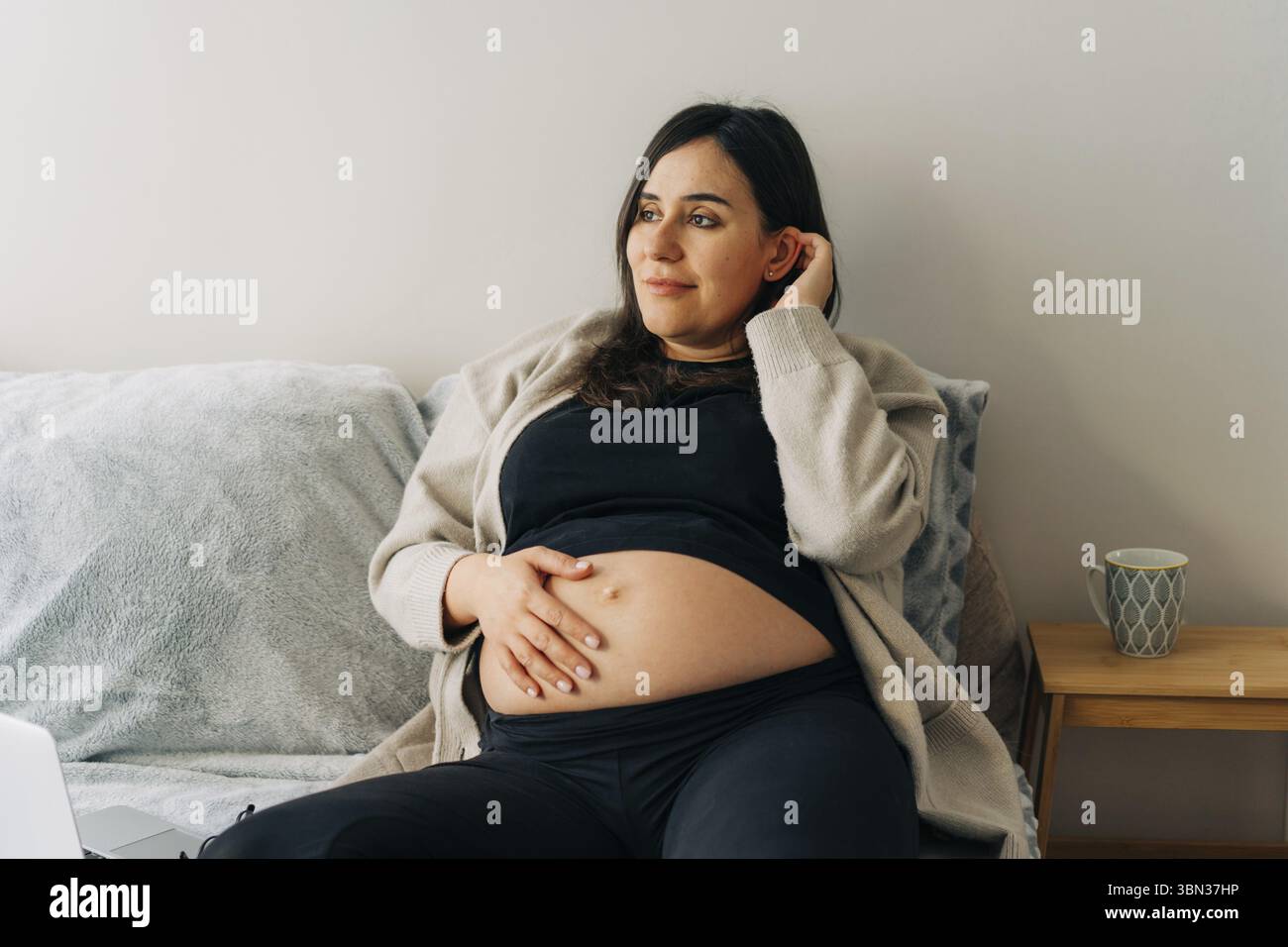 Schwangere werdende attraktive Frau sitzt in Vergnügen auf der Couch Stockfoto