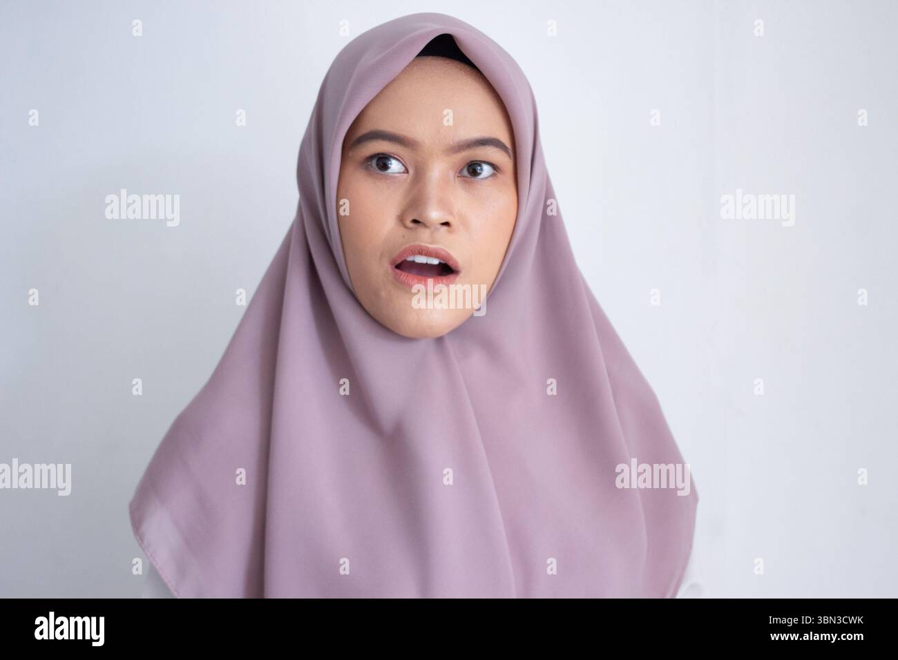 Junge asiatische muslime, die einen violetten Hijab trägt, lila Schal mit weit geöffneten Augen. Der Schal bedeckt ihren Kopf und Hals Stockfoto