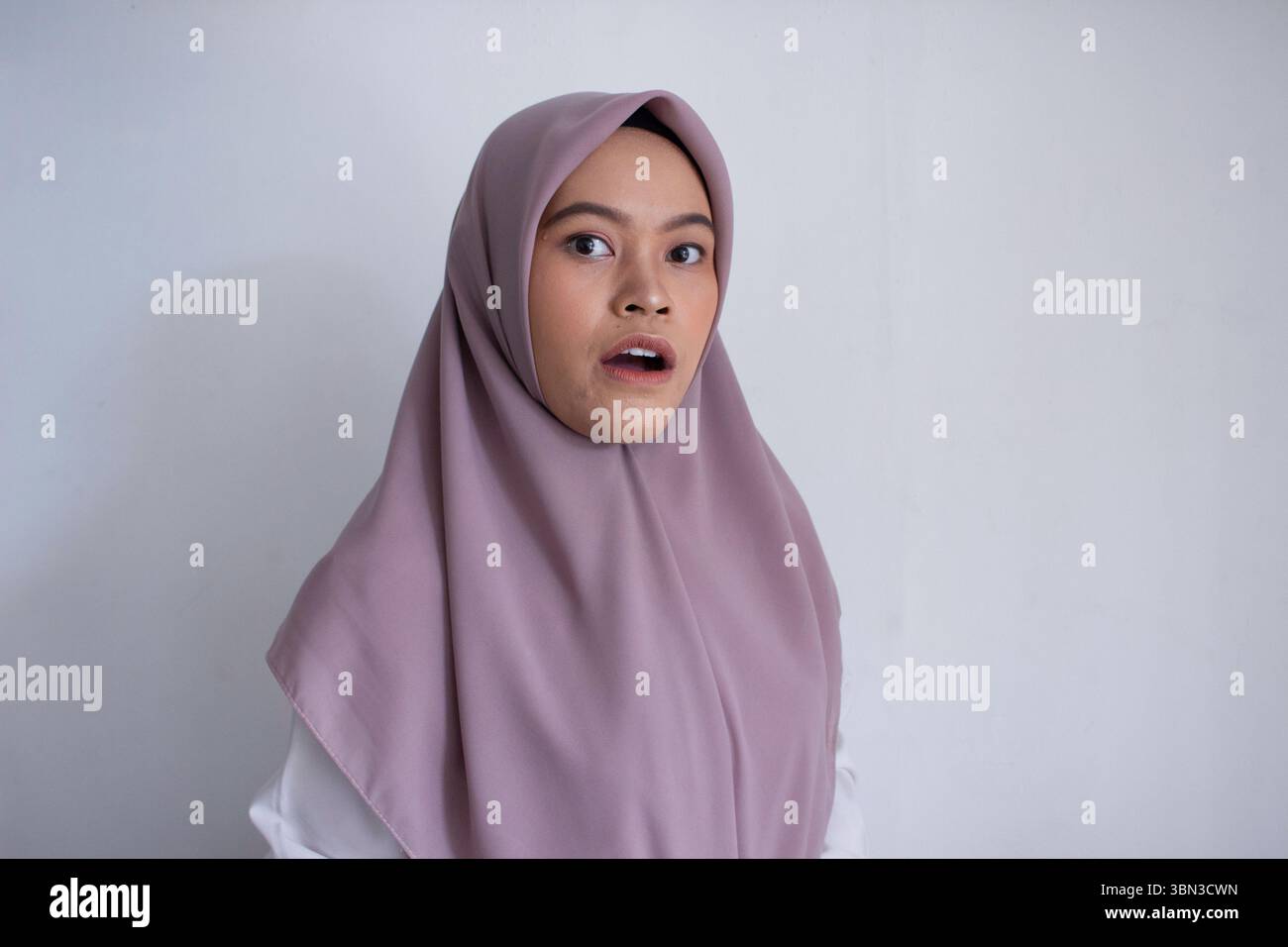 Junge asiatische muslime, die einen violetten Hijab trägt, lila Schal mit weit geöffneten Augen. Der Schal bedeckt ihren Kopf und Hals Stockfoto