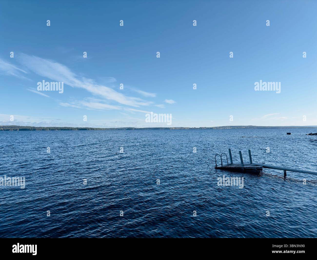 Der hellblaue Himmel trifft auf das ruhige Wasser eines riesigen Sees an einem sonnigen Tag, nördlich von Schweden Stockfoto