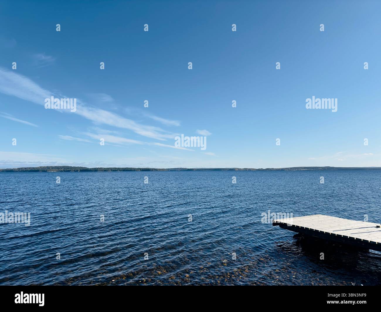 Der hellblaue Himmel trifft auf das ruhige Wasser eines riesigen Sees an einem sonnigen Tag, nördlich von Schweden Stockfoto