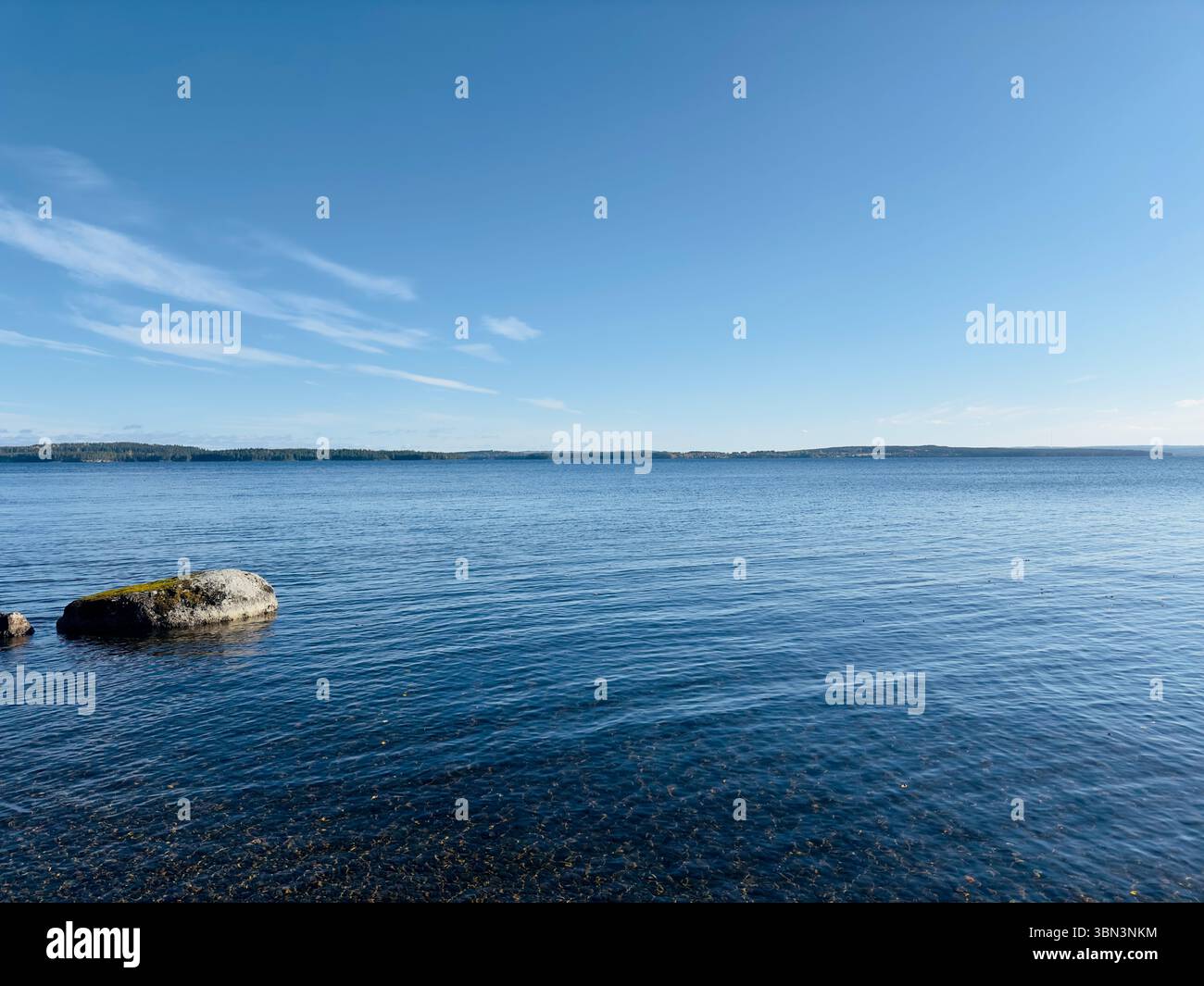 Der hellblaue Himmel trifft auf das ruhige Wasser eines riesigen Sees an einem sonnigen Tag, nördlich von Schweden Stockfoto