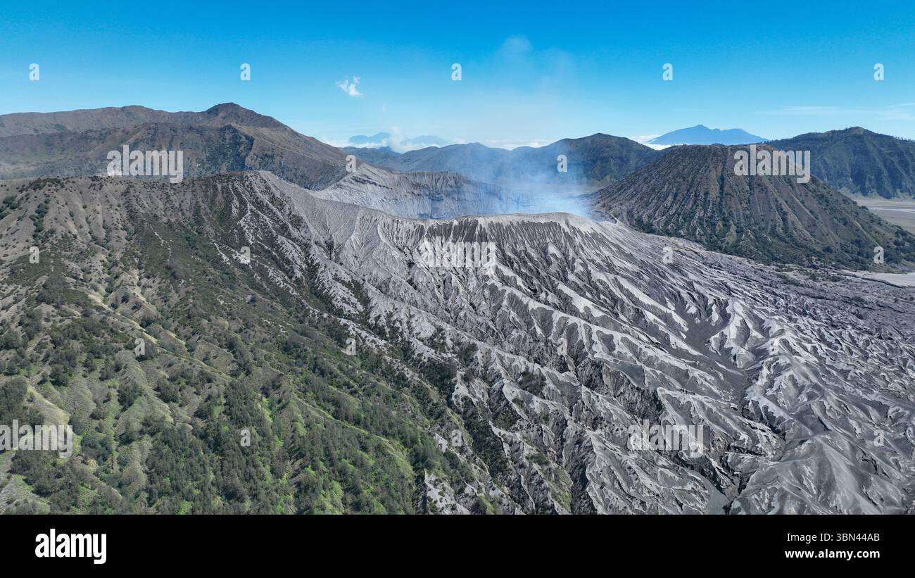 Ein beeindruckender Drohnenschuss fängt die zerklüfteten Hänge eines aktiven Vulkans mit Rauch ein, der aus seinem Krater steigt. Markanter Kontrast zwischen aschüberzogener Oberfläche Stockfoto