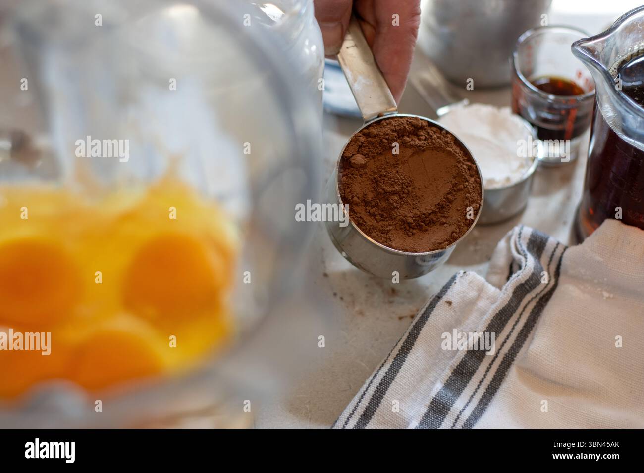 Kakaopulver neben zerbrochenen Eiern im Mixbecher Stockfoto