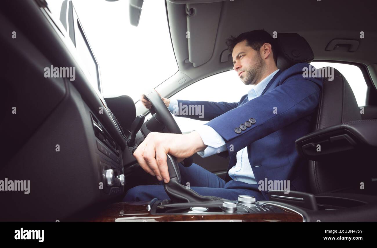 Geschäftsmann bedient Lenkrad und Schalthebel in einem flachen Fahrzeug mit Infotainment-Bildschirm Stockfoto