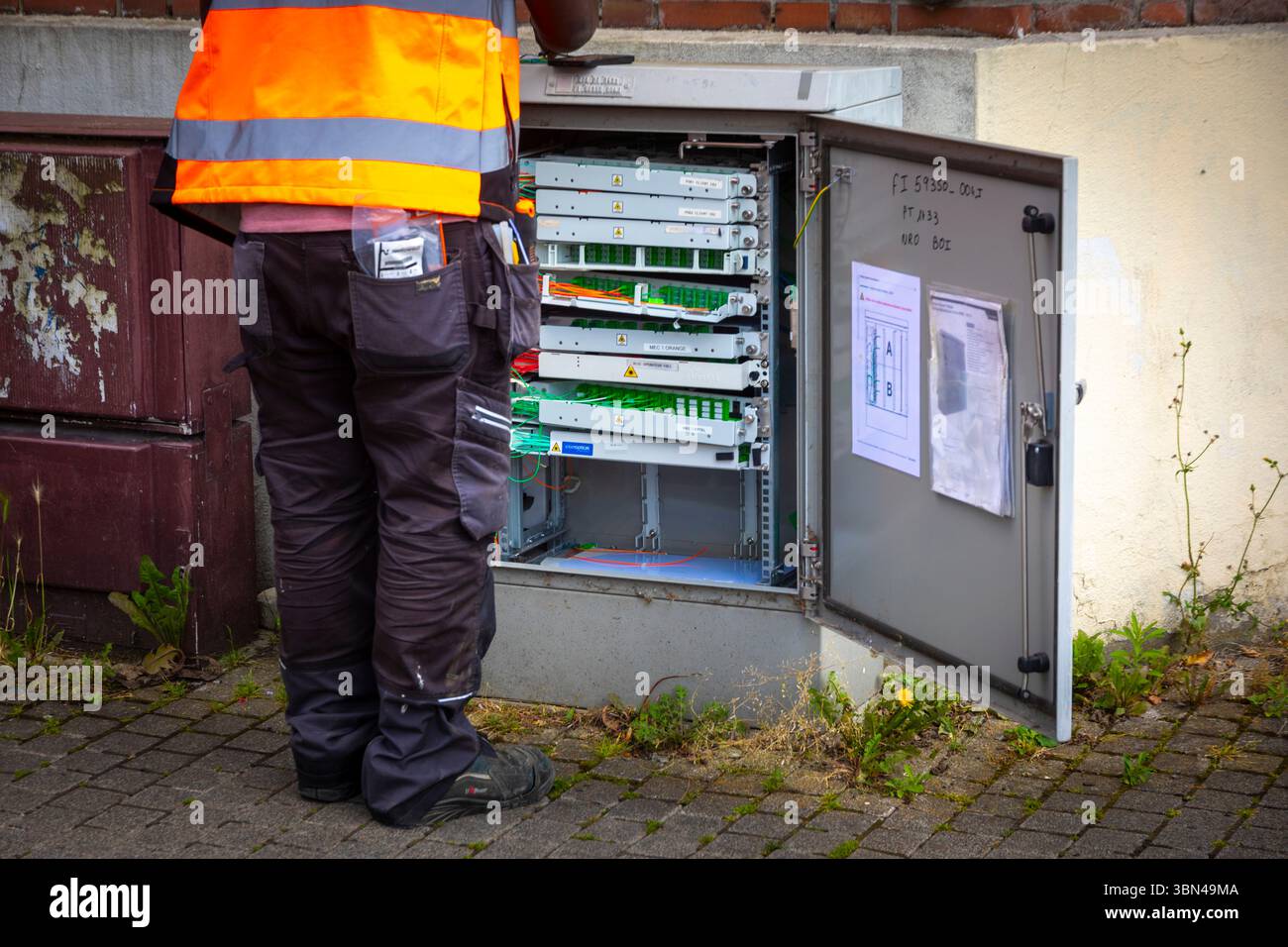 Mitarbeiter, der an einem Glasfaser-Straßenschrank, einem Glasfaser-Verteilerrahmen oder einem Glasfaser-SRO (für optischen Unterverteiler) arbeitet Stockfoto