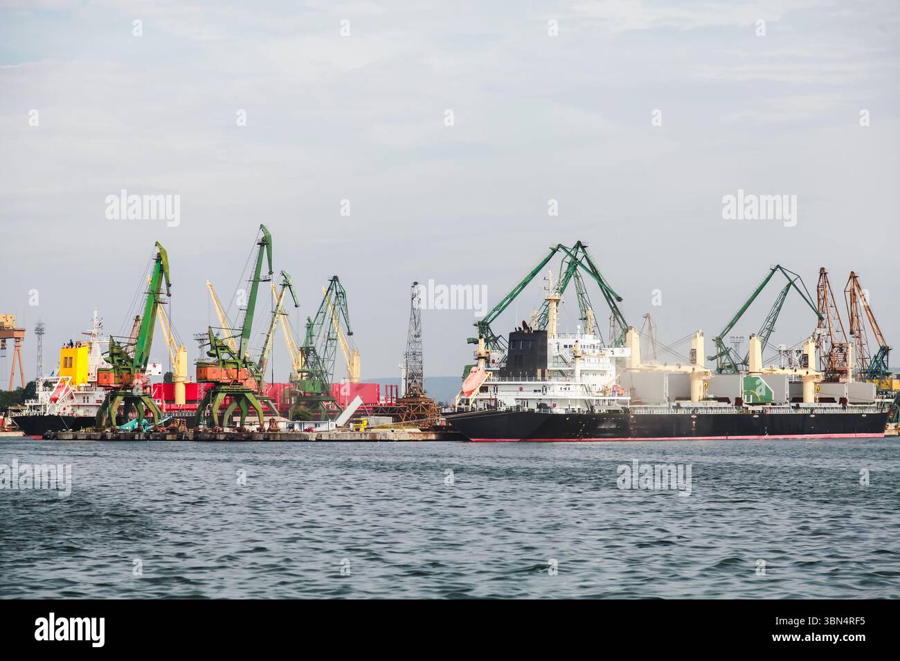Frachtschiffe, die an einem Industriehafen angedockt sind, umgeben von zahlreichen Kränen und Ausrüstungen, die zum Be- und Entladen von Gütern verwendet werden. Varna, Bulgarien Stockfoto
