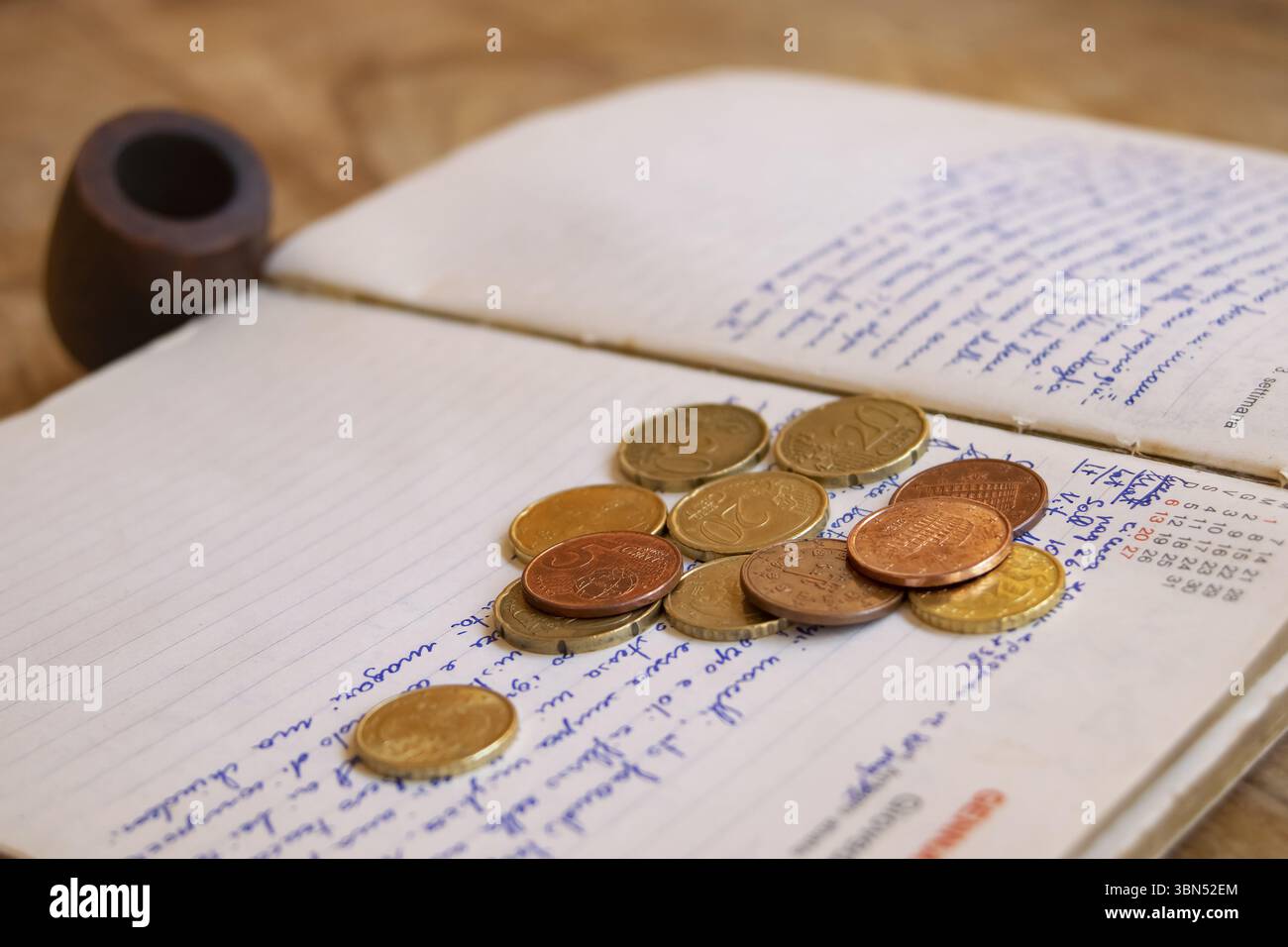 Auf den Seiten einer veralteten, handschriftlichen Zeitschrift liegen verstreute Euro-Münzen, die auf persönliche Finanzen oder vergangene Ausgaben hindeuten Stockfoto