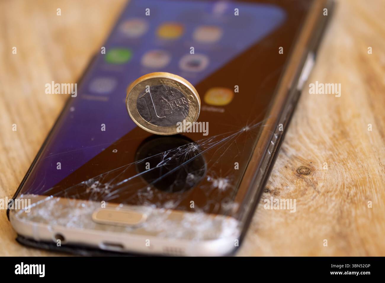 Euro-Münze auf einem zerrissenen Smartphone-Bildschirm, die wirtschaftlichen Wert im Vergleich zu zerbrechlicher oder veralteter Technologie symbolisiert. Digital Decay Conep Stockfoto