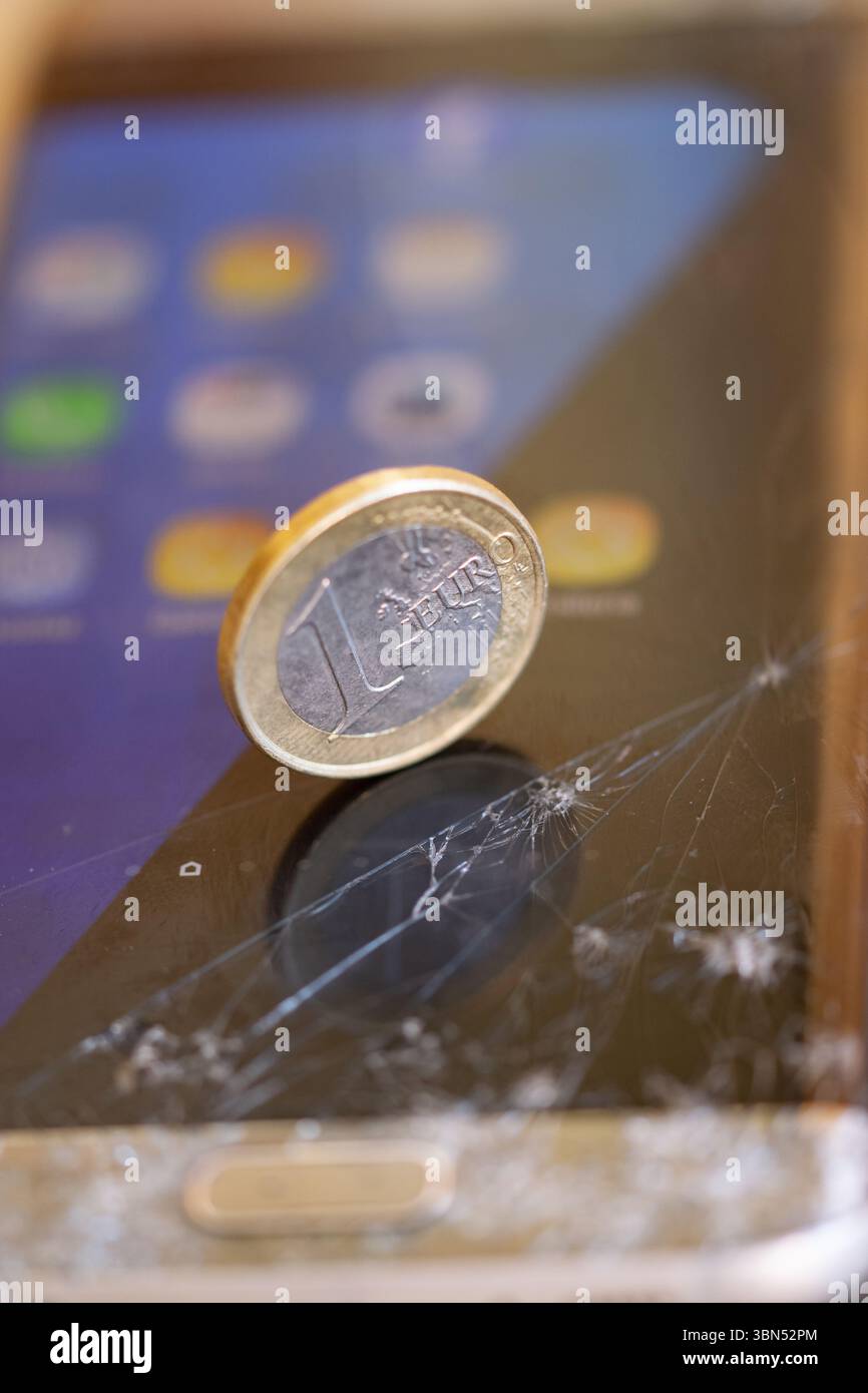 Euro-Münze auf einem zerrissenen Smartphone-Bildschirm, die wirtschaftlichen Wert im Vergleich zu zerbrechlicher oder veralteter Technologie symbolisiert. Digital Decay Conep Stockfoto