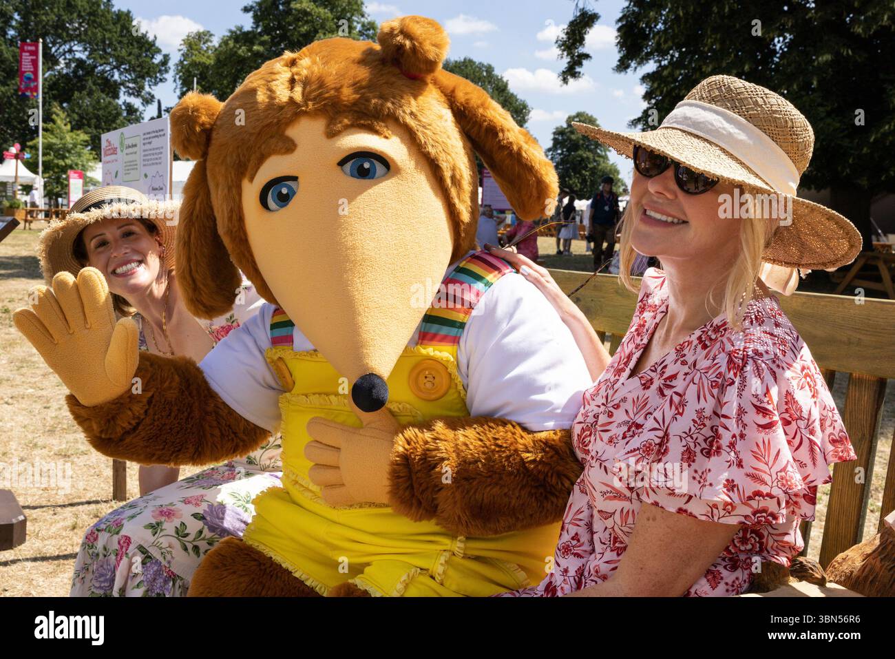 Hampton Court Palace, Surrey, Großbritannien. 30. Juni 2025. Womble Alderney von The Wombles posiert mit zwei jungen Damen und einer Womble Show, während er sich auf einer Bank ausruhen, um sich an diesem heißen Sommertag abzukühlen. Prominente und Pressebesucher genießen das Blumenfest. Wunderschöne Gartendesigns, Produkte und Blumendekorationen werden vom 1. Bis 6. Juli auf dem HAMPTON Court Palace Garden Festival gezeigt. Quelle: Imageplotter/Alamy Live News Stockfoto