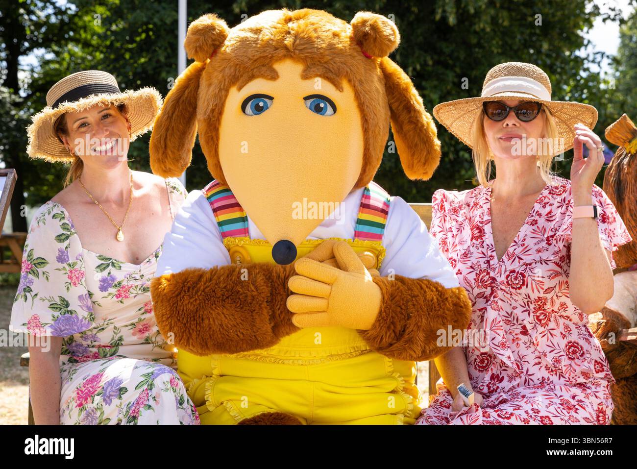 Hampton Court Palace, Surrey, Großbritannien. 30. Juni 2025. Womble Alderney von The Wombles posiert mit zwei jungen Damen und einer Womble Show, während er sich auf einer Bank ausruhen, um sich an diesem heißen Sommertag abzukühlen. Prominente und Pressebesucher genießen das Blumenfest. Wunderschöne Gartendesigns, Produkte und Blumendekorationen werden vom 1. Bis 6. Juli auf dem HAMPTON Court Palace Garden Festival gezeigt. Quelle: Imageplotter/Alamy Live News Stockfoto