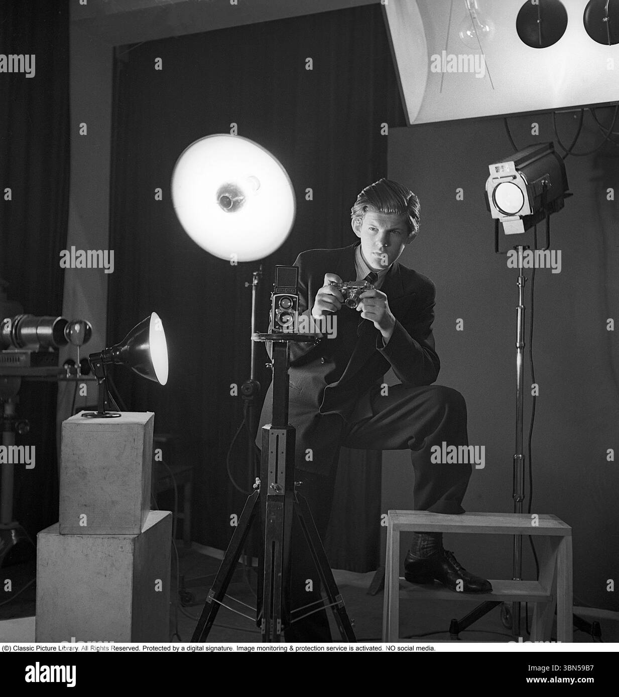 Pressphotograf der 1940er Jahre Anders Swahn stellte eine Kamera in der Hand und posierte für ein Foto in einem Fotostudio mit Lichtern. Eine Rolleiflex-Kamera ist auf dem Stativ vor ihm montiert. Eine Standardausrüstung für Pressefotografen zu dieser Zeit. 1948. Anders Svahn Stockfoto