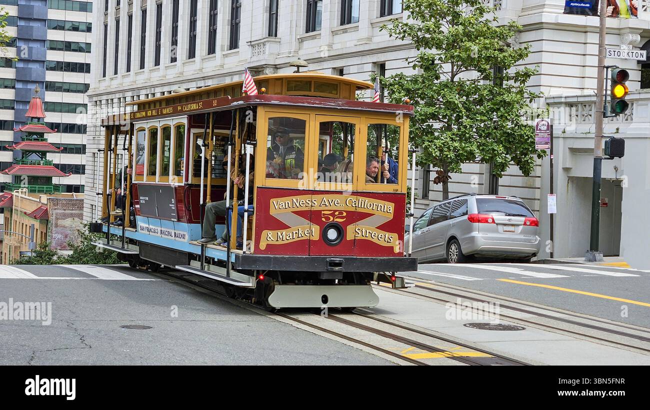 Die berühmte Seilbahn von San Francisco führt über eine steile Stadtstraße, umgeben von farbenfrohen Häusern und urbanem Leben Stockfoto