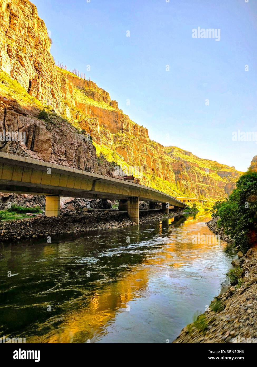 Der friedliche Fluss schlängelt sich durch ein üppiges, sonniges Tal mit weichen Wolken und Bergkulissen in Colorado. - Smartphone-aufgenommenes Stockfoto