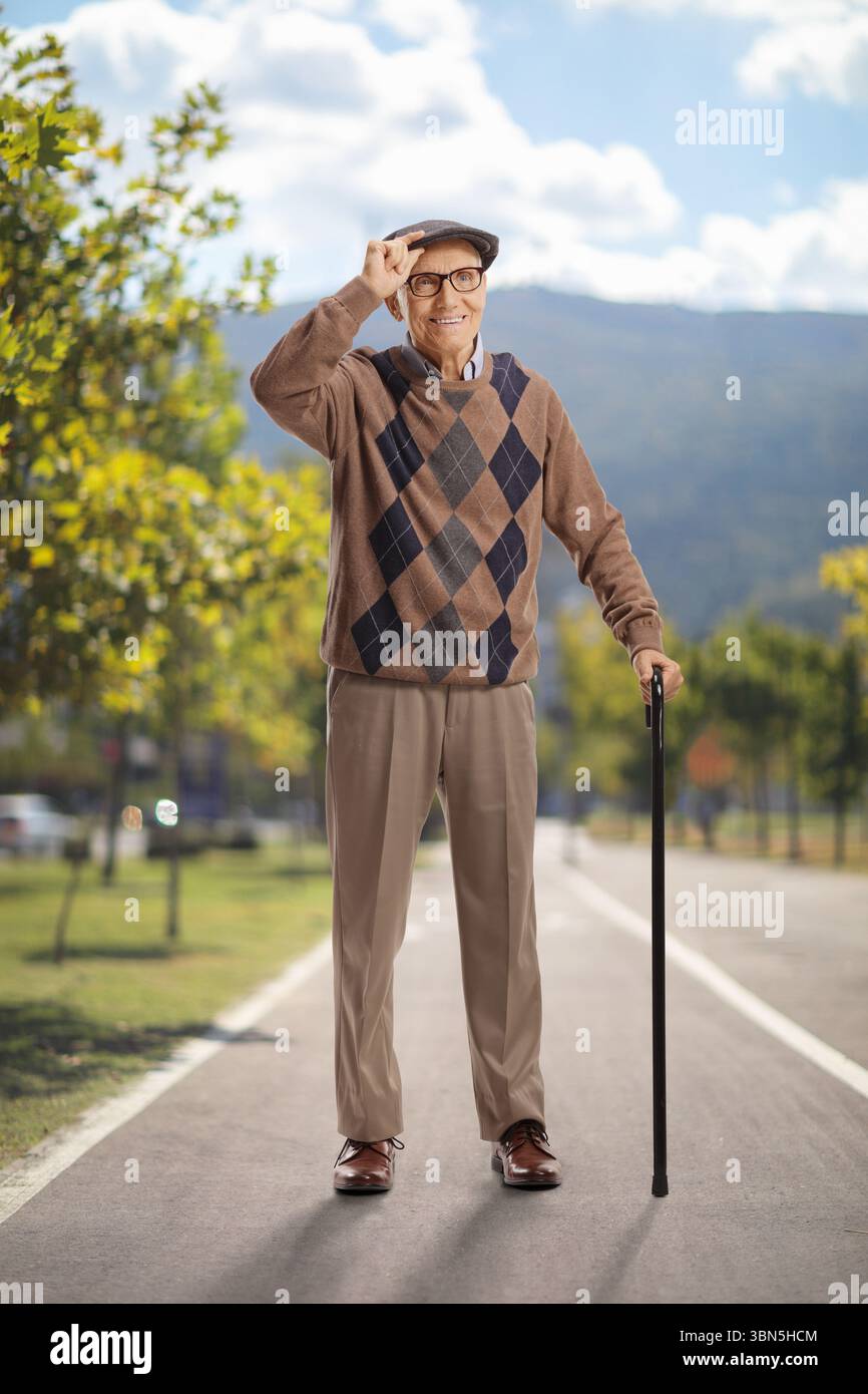 Seniorenmann mit Gehstock im Park, Begrüßung mit Hut Stockfoto