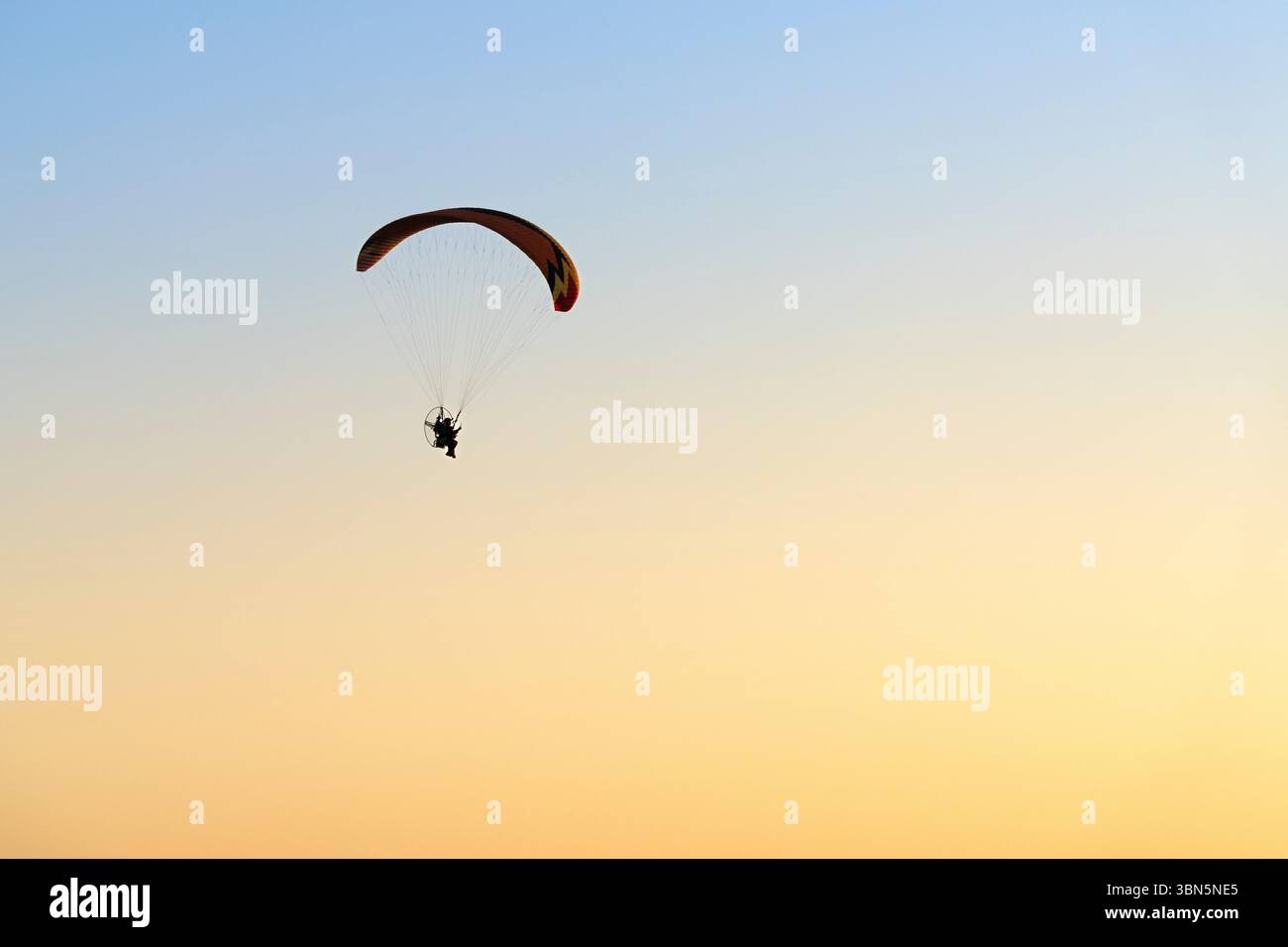 Einsame Gleitschirmflieger fliegen über einen leuchtend orange-gelben Sonnenaufgangshimmel über Alice Springs, Australien. Horizontales Bild mit reichlich Kopierraum. Stockfoto