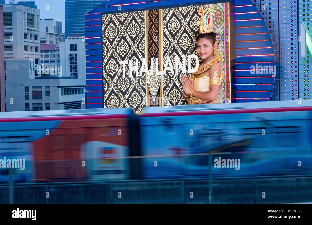 Verschwommene Stadtbahn vorbei an einer digitalen Werbetafel mit einer wunderschönen Frau in traditioneller thailändischer Tracht, Bangkok, Thailand Stockfoto