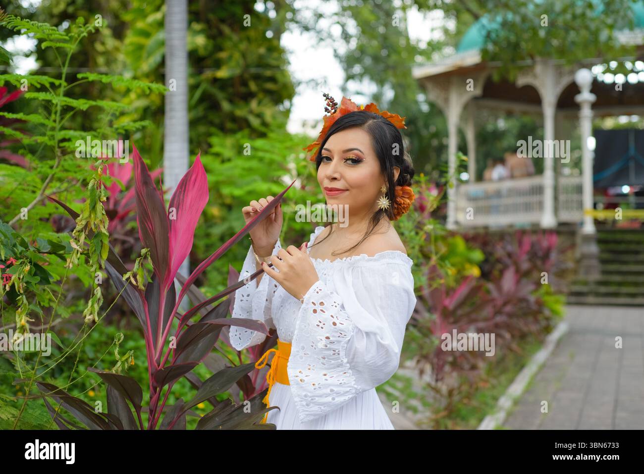 Eine Frau in einem schulterfreien Kleid mit weißem Ösen, verziert mit einem Kopfschmuck mit Blattmotiv und goldenen Ohrringen Stockfoto
