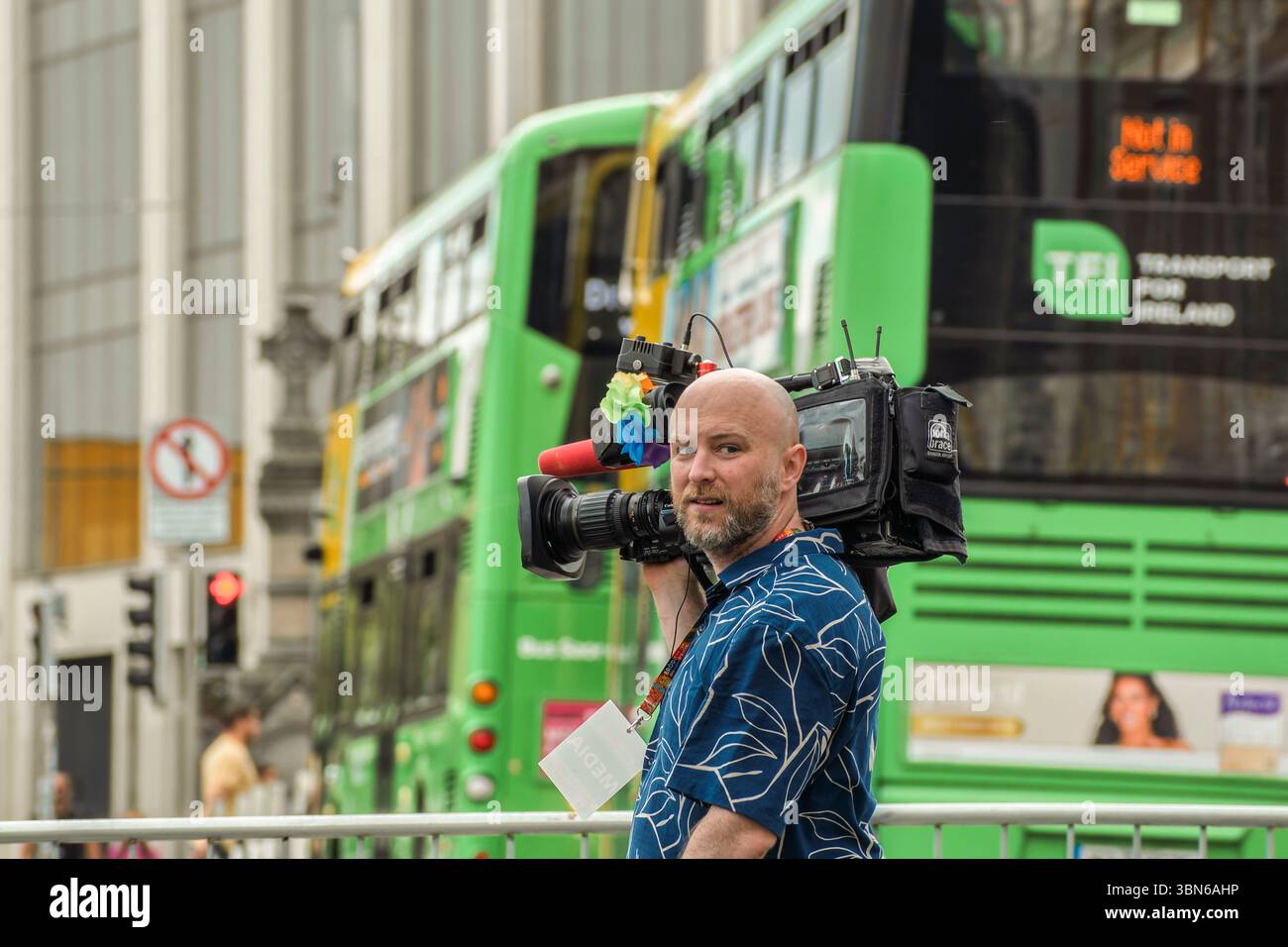 Professioneller Kameramann filmt auf einer geschäftigen Stadtstraße mit einem grünen Dublin-Bus im Hintergrund, 28. Juni 2025 Stockfoto