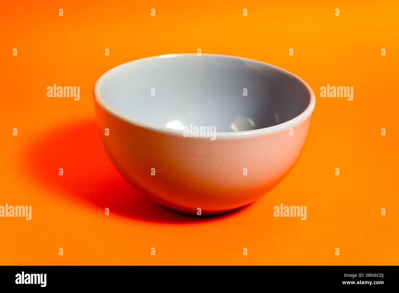 Einfache graue Schüssel auf leuchtendem orangefarbenem Hintergrund für starken Kontrast und Schatten Stockfoto