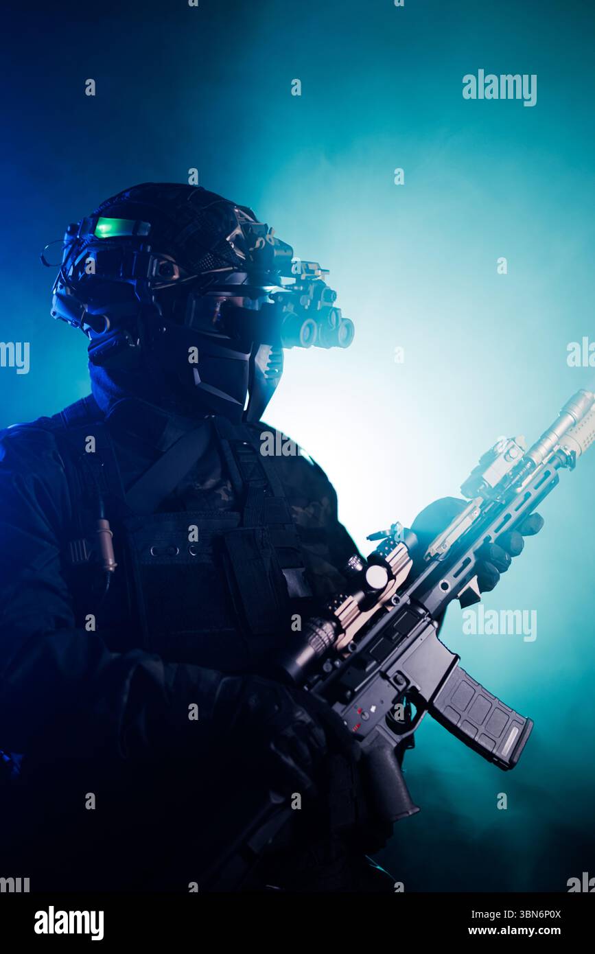 Bewaffneter Agent in taktischer Ausrüstung, mit Nachtsichtgeräten und in einer blauen, intensiven Szene mit dramatischer Beleuchtung, die das Atmosp verstärkt Stockfoto