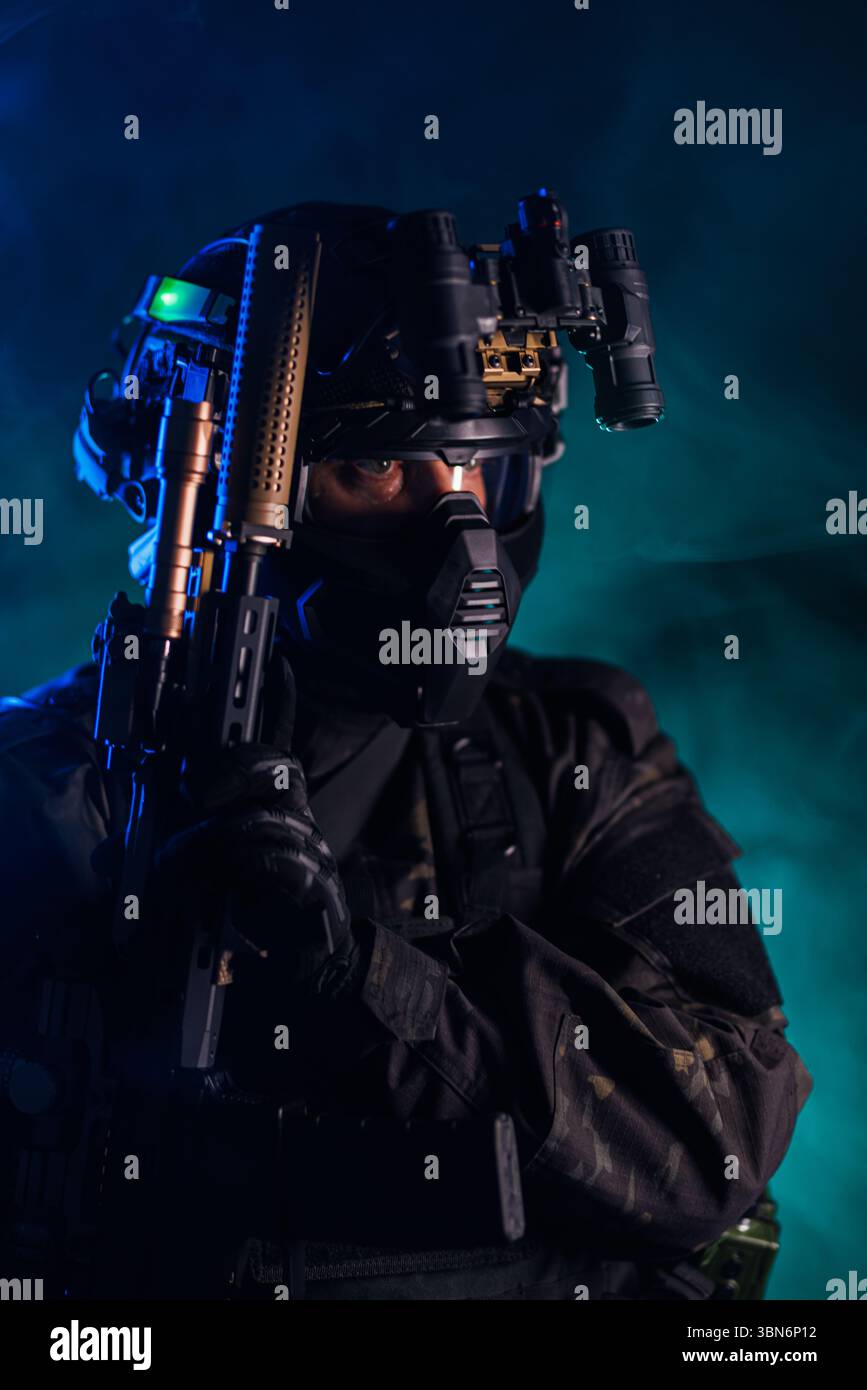 Taktischer Agent in schwarzem Gewand mit Nachtsichtbrille und Gewehr im atmosphärischen Rauch, der an Themen wie Tarnung, Strategie und modernes Wa erinnert Stockfoto