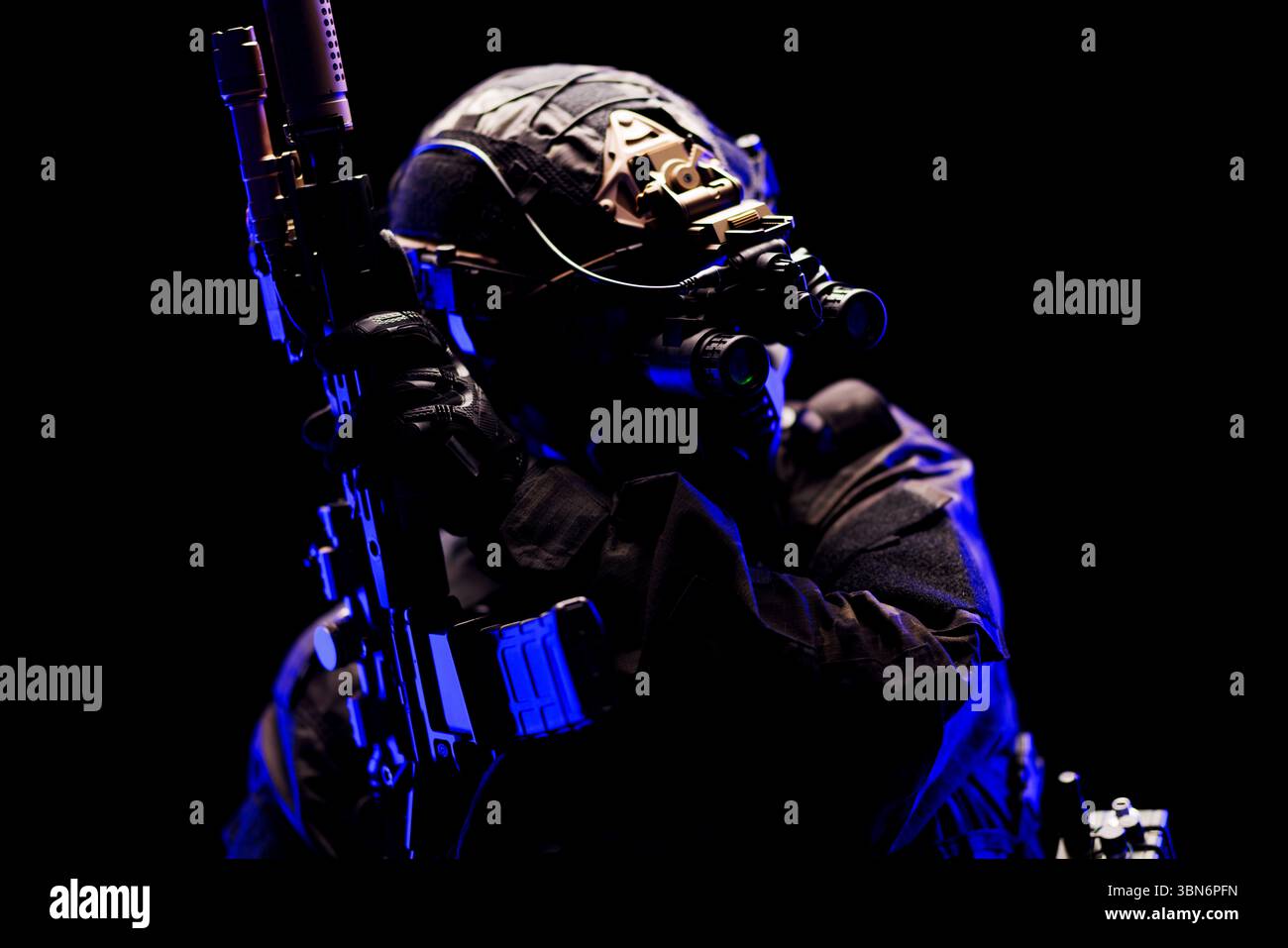 Taktischer Soldat in schwarzer Uniform, ausgestattet mit Nachtsichtbrille, der bei schlechten Lichtverhältnissen eine Schusswaffe bedient. Zeigt Themen der Kriegsführung, Stockfoto